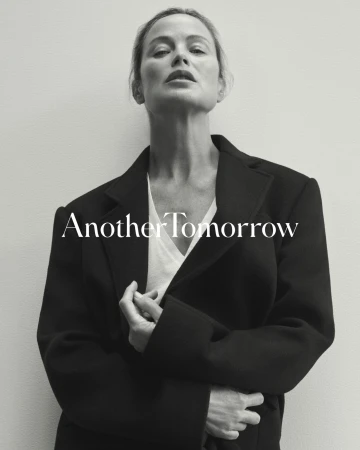 Adult woman in a black jacket and white top poses in front of a gray wall with the text 'Another Tomorrow' overlaid.