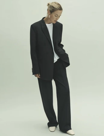 A woman posing in a studio wearing a black blazer, white t-shirt, and black pants in a fashion editorial shot.