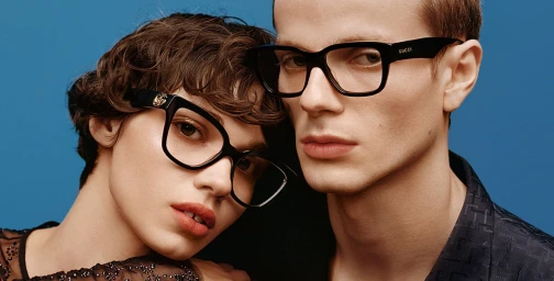 Close-up portrait of two models wearing black Gucci eyewear against a solid blue background