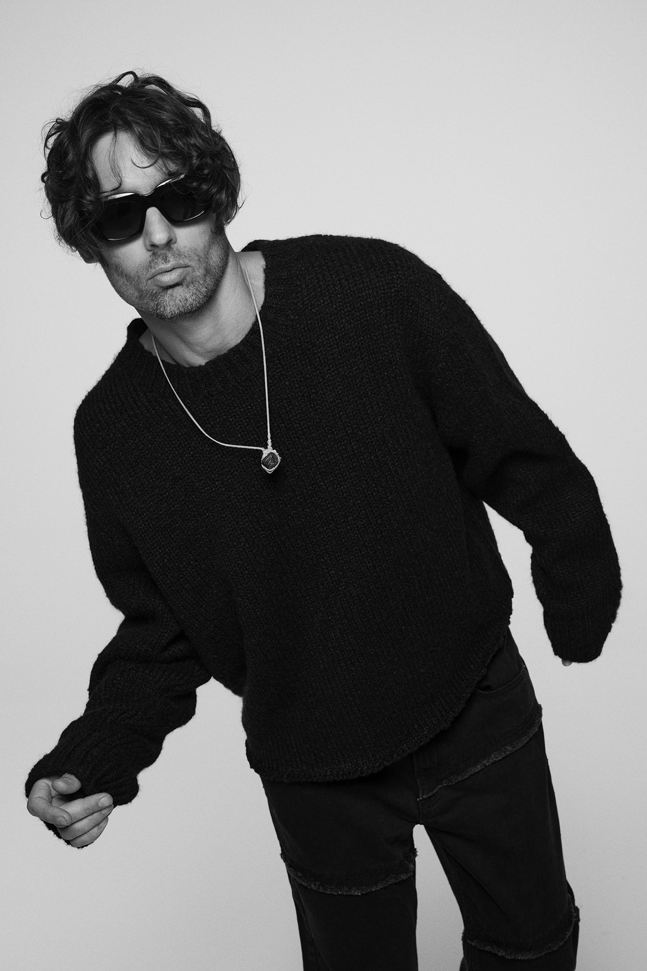 Black and white portrait of adult male wearing a knit sweater and sunglasses, staring at the camera against a plain background.