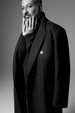 Monochrome portrait of a man wearing a dark double-breasted coat and touching his face in studio lighting