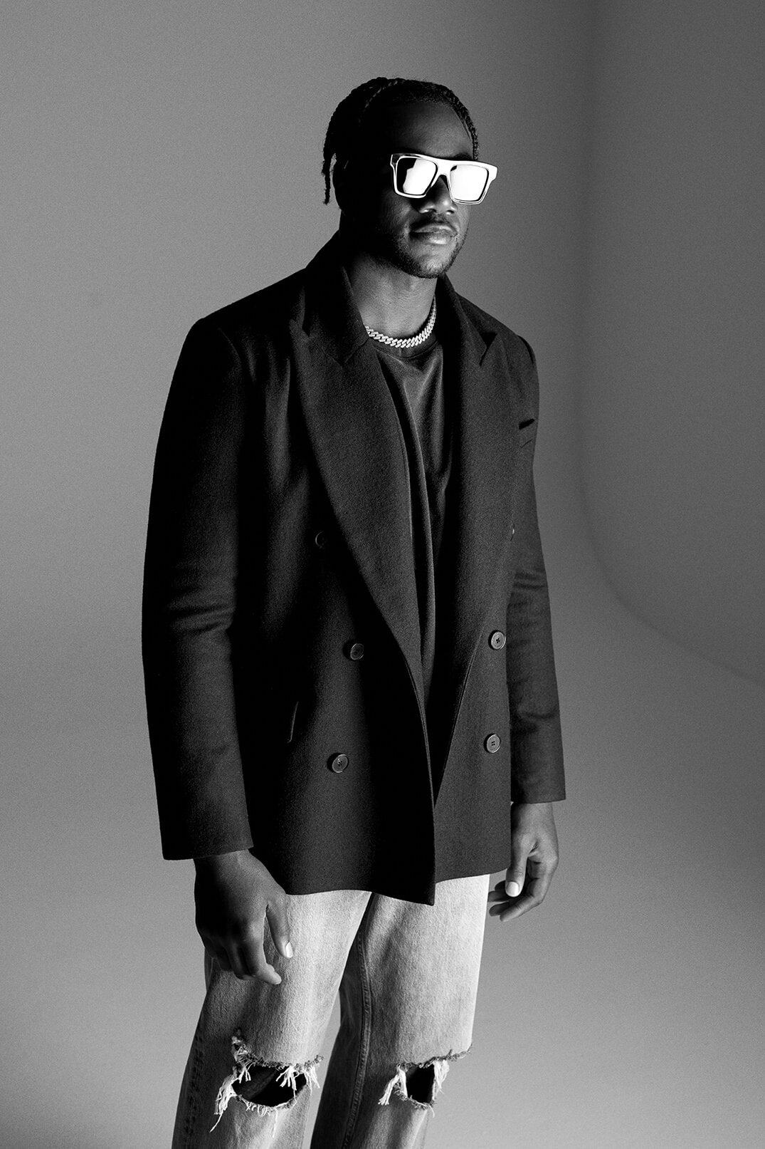Portrait of a Black male model in a black blazer and distressed jeans, posing in a photo studio with neutral gray background.