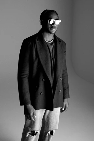 Portrait of a Black male model in a black blazer and distressed jeans, posing in a photo studio with neutral gray background.