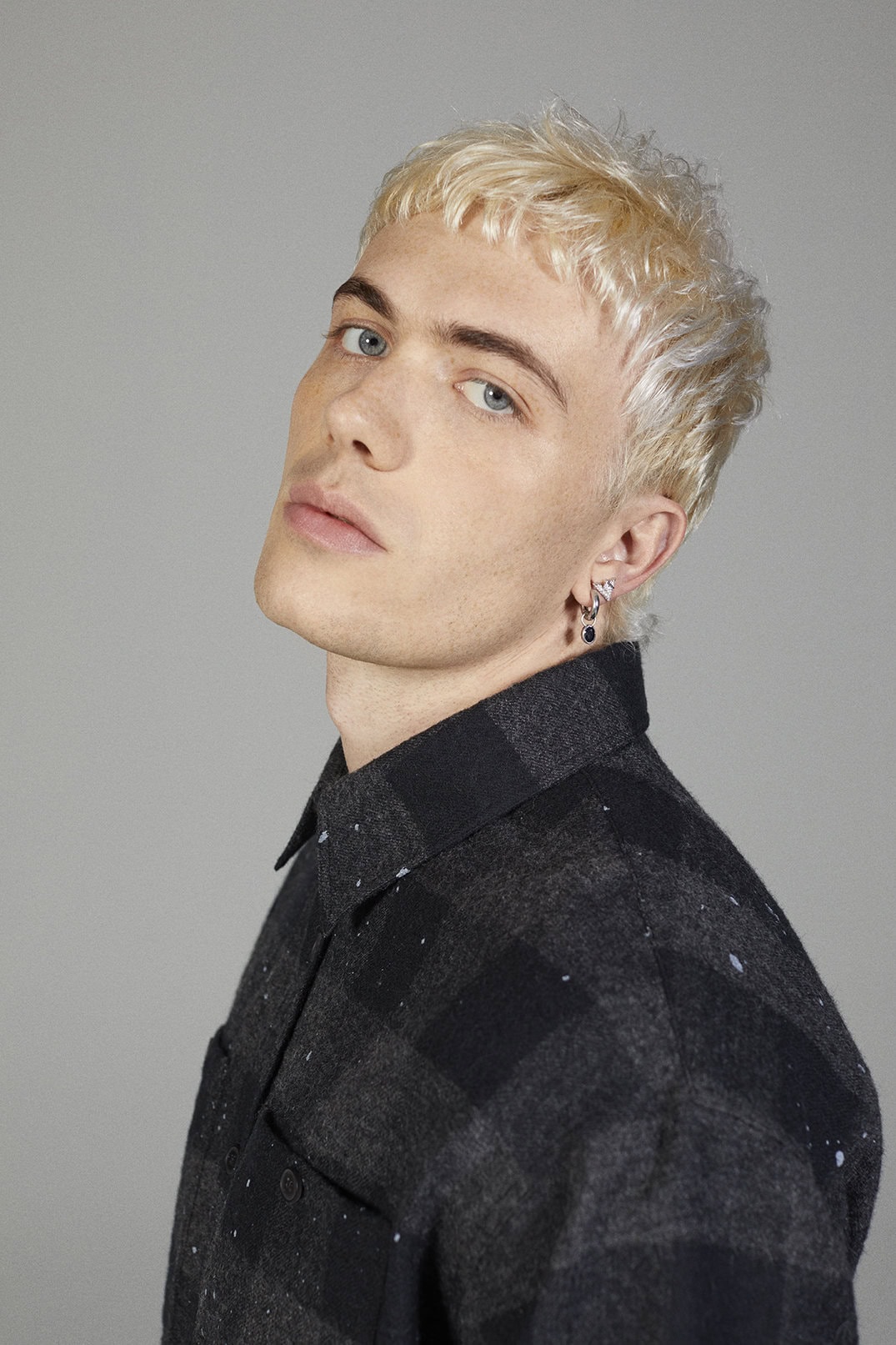 Portrait of a blonde man wearing a dark plaid shirt against a solid grey background