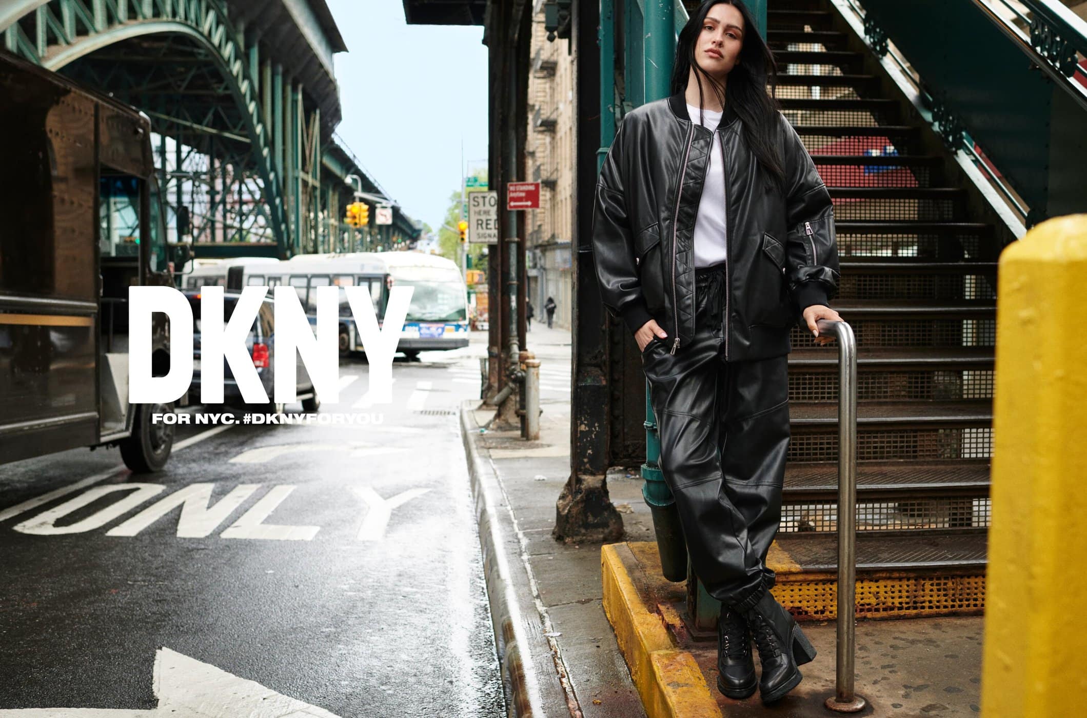 Amelia Gray Hamlin wearing a black leather jacket and matching pants standing near an elevated subway staircase in New York City.