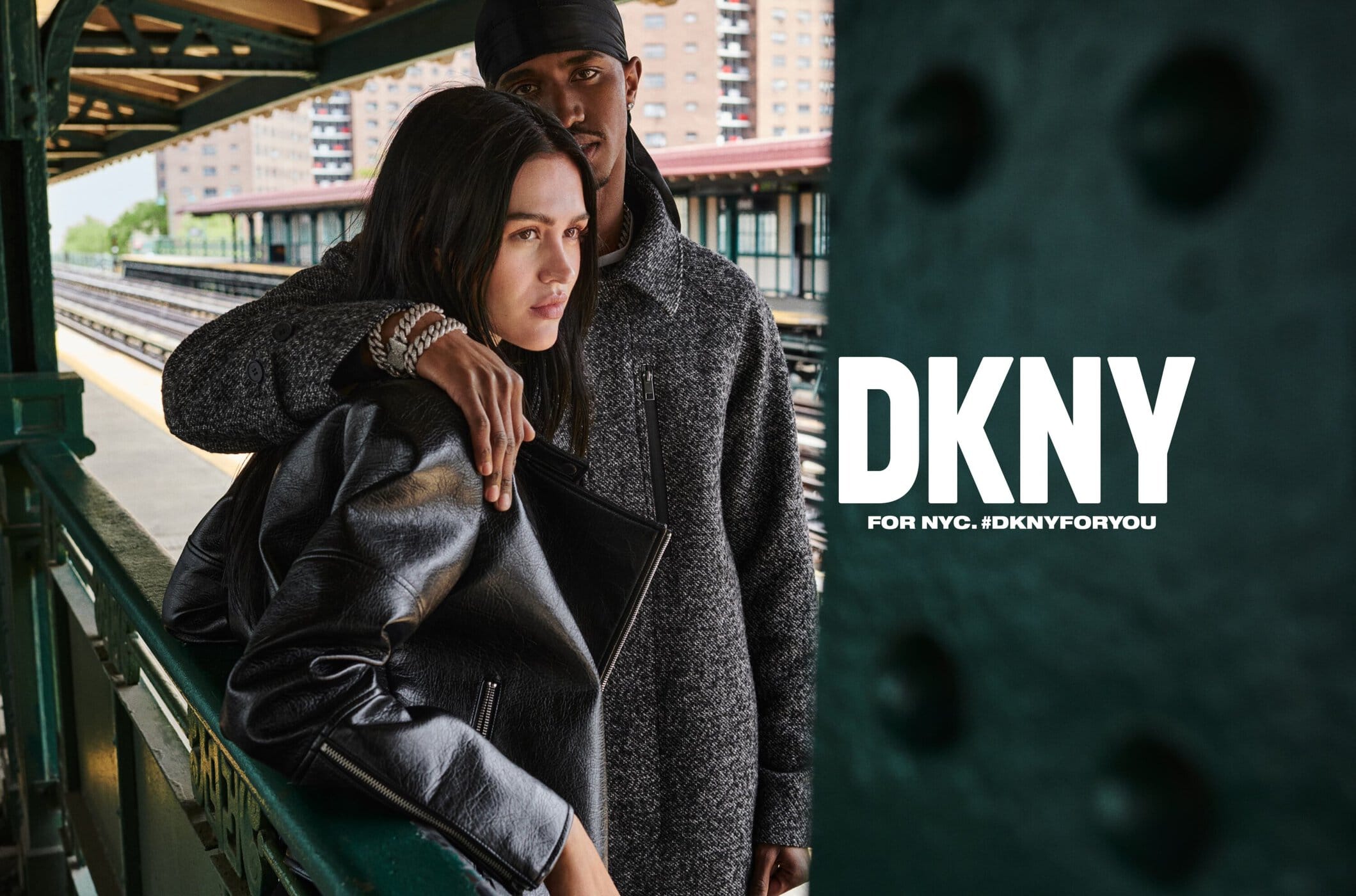 Fashion ad featuring a couple on a subway platform. The woman wears a leather jacket and the man a gray coat. The DKNY logo is displayed.