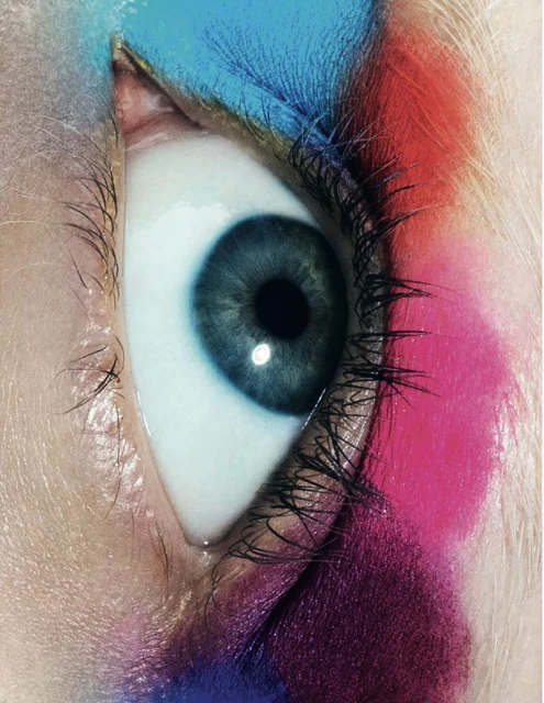 Close-up of a grey-blue eye with colorful makeup in shades of blue, red, and purple, creating a vibrant and artistic beauty image.