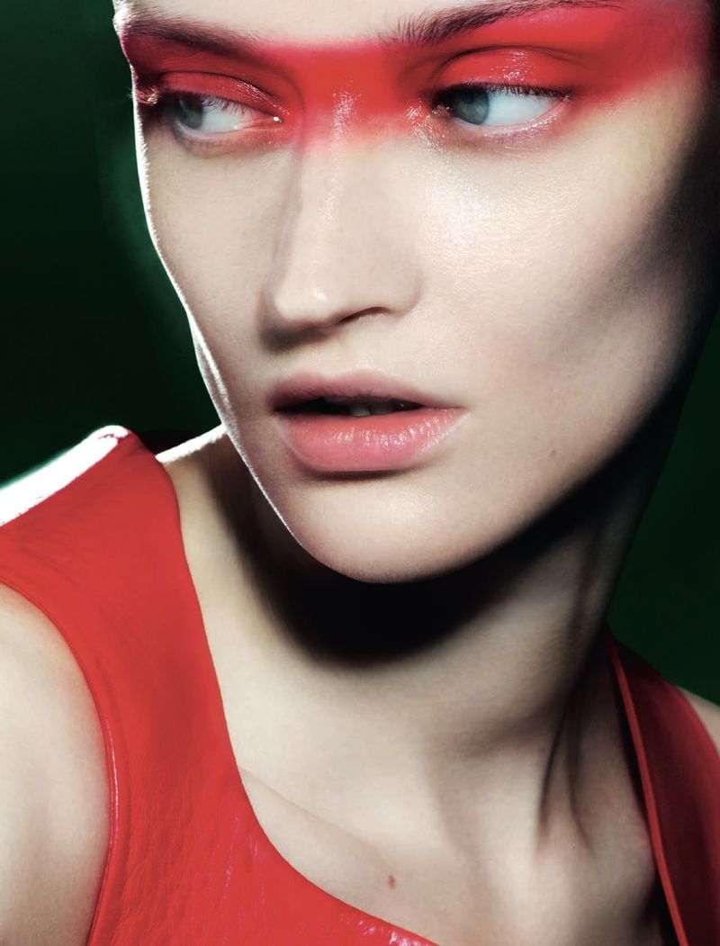 Close-up portrait of a fair-skinned young woman with bright blue eyes and bold red makeup on her eyelids and forehead, looking away.