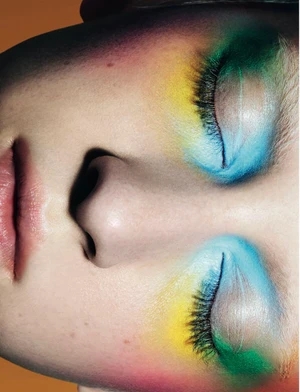 Close-up portrait of a model with vibrant rainbow eye makeup featuring blue and yellow tones for Vogue Greece by Sabine Villiard.