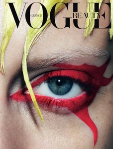 Close-up portrait of a model's eye with striking red graphic eyeliner and yellow wet-look hair for Vogue Greece.