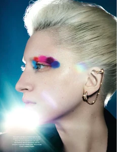 Close-up profile of a blonde model with colorful eyeshadow and gold ear cuff against a blue background for Vogue Greece.