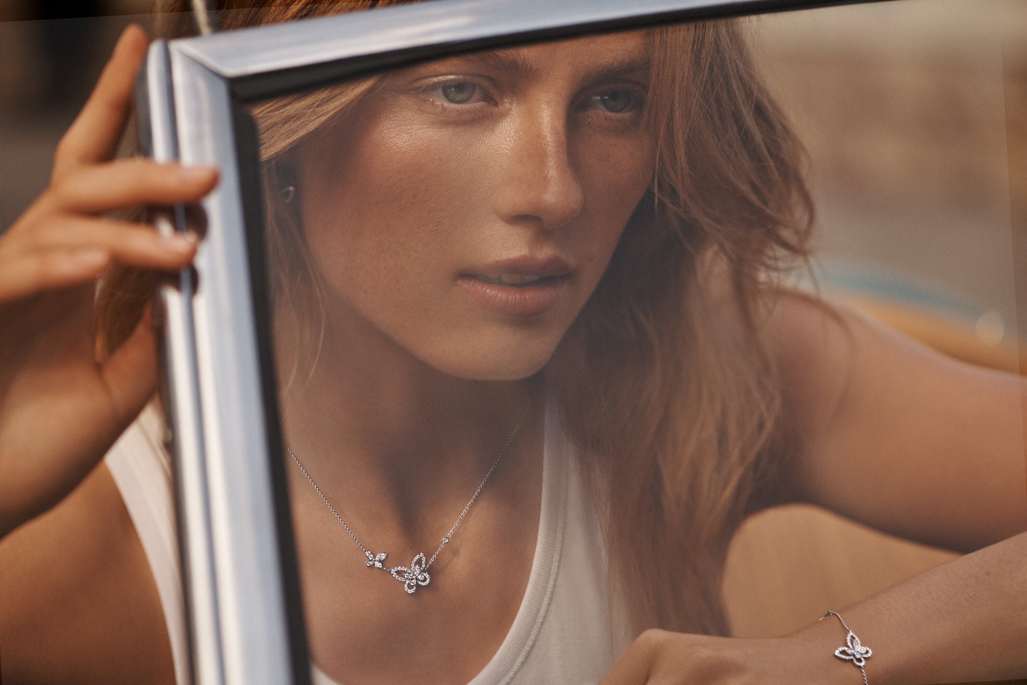 Adult female model poses in a car wearing silver butterfly necklace and bracelet, medium shot, outdoor fashion jewelry advertisement.