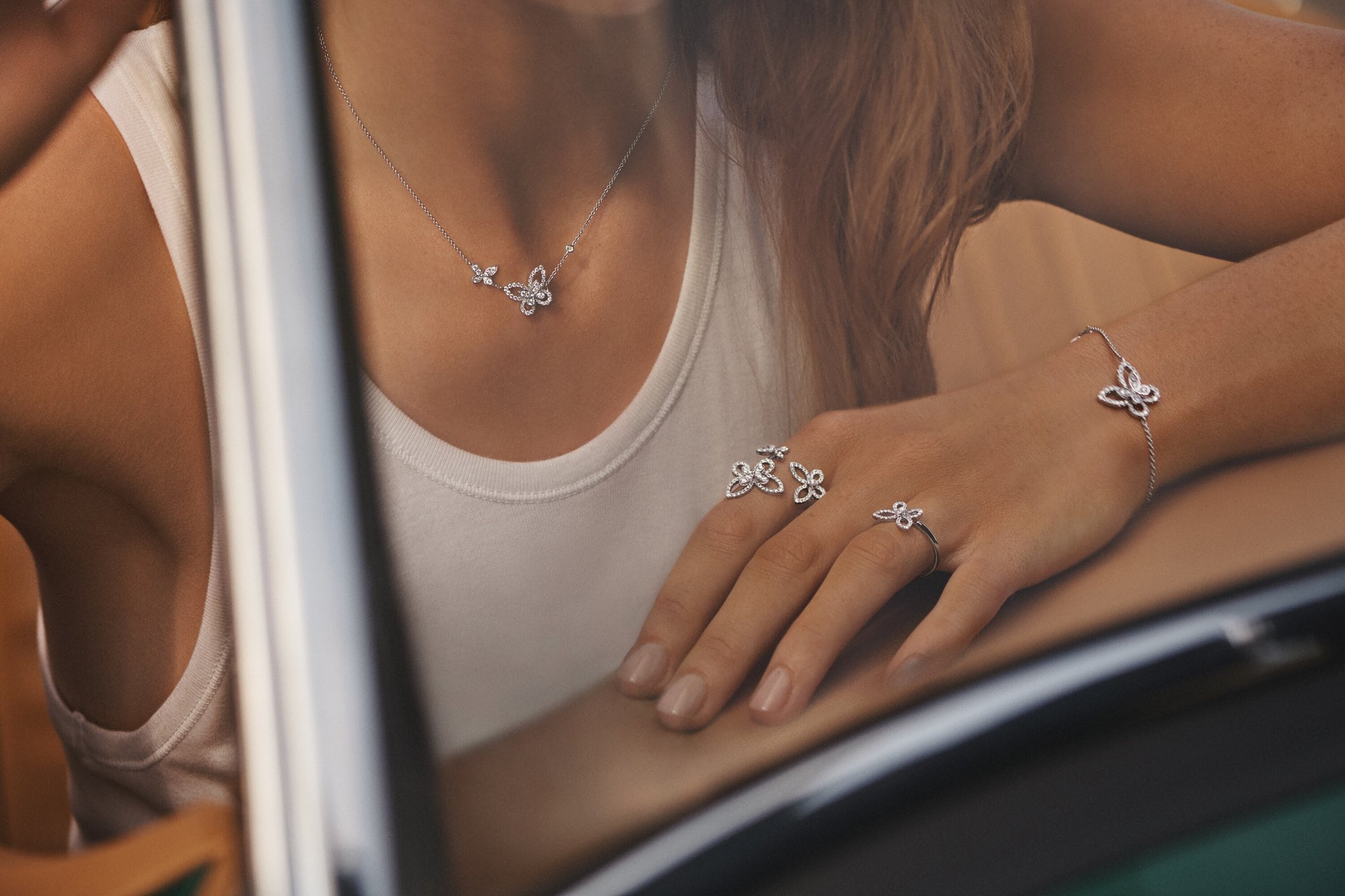Woman showcases butterfly jewelry set featuring a necklace, ring, and bracelet, silver color on a tanned skin, against car interior.