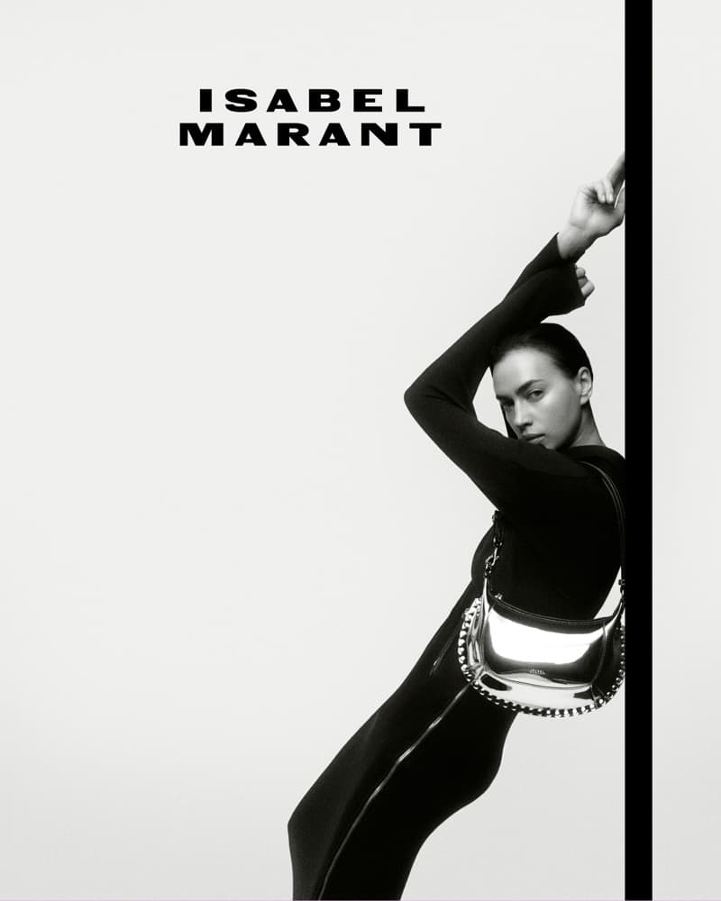 Fashion shot of a woman in a long-sleeved black dress with a metallic silver purse, set against a bright white backdrop.