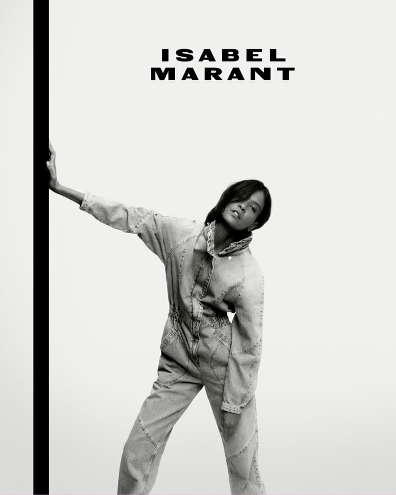 Fashion shot: a black-haired woman in a denim jumpsuit poses near a black vertical bar with the brand Isabel Marant at the top of the frame.