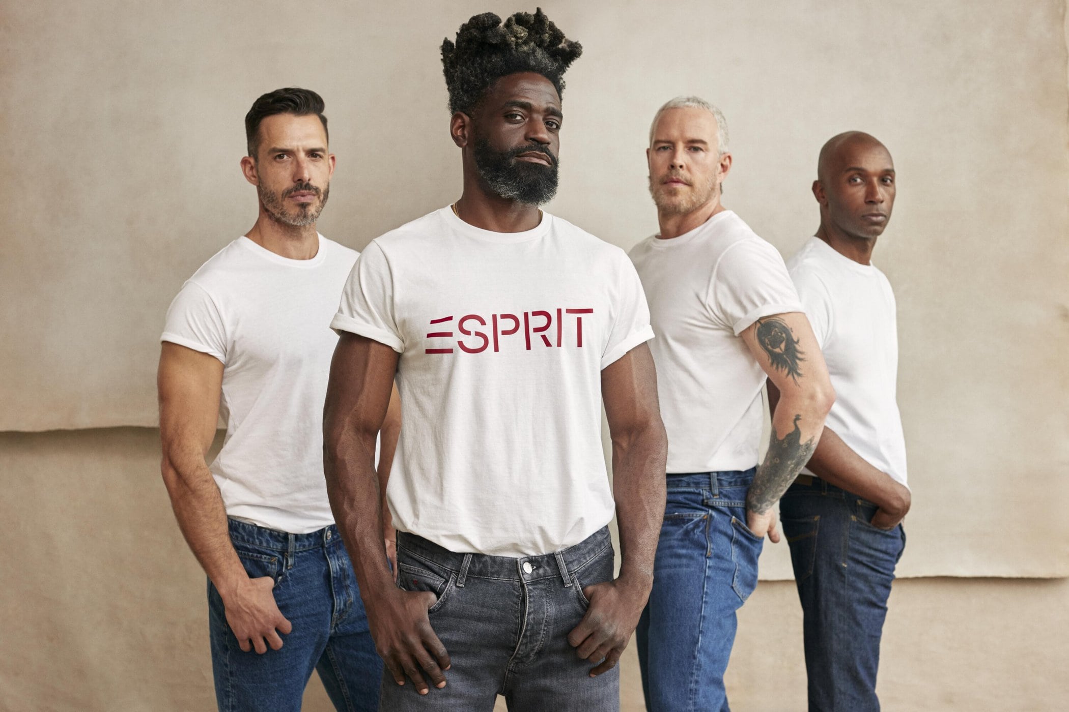 Group of diverse men in white t-shirts and jeans posing against a textured backdrop; focus on the man in the 'Esprit' tee.