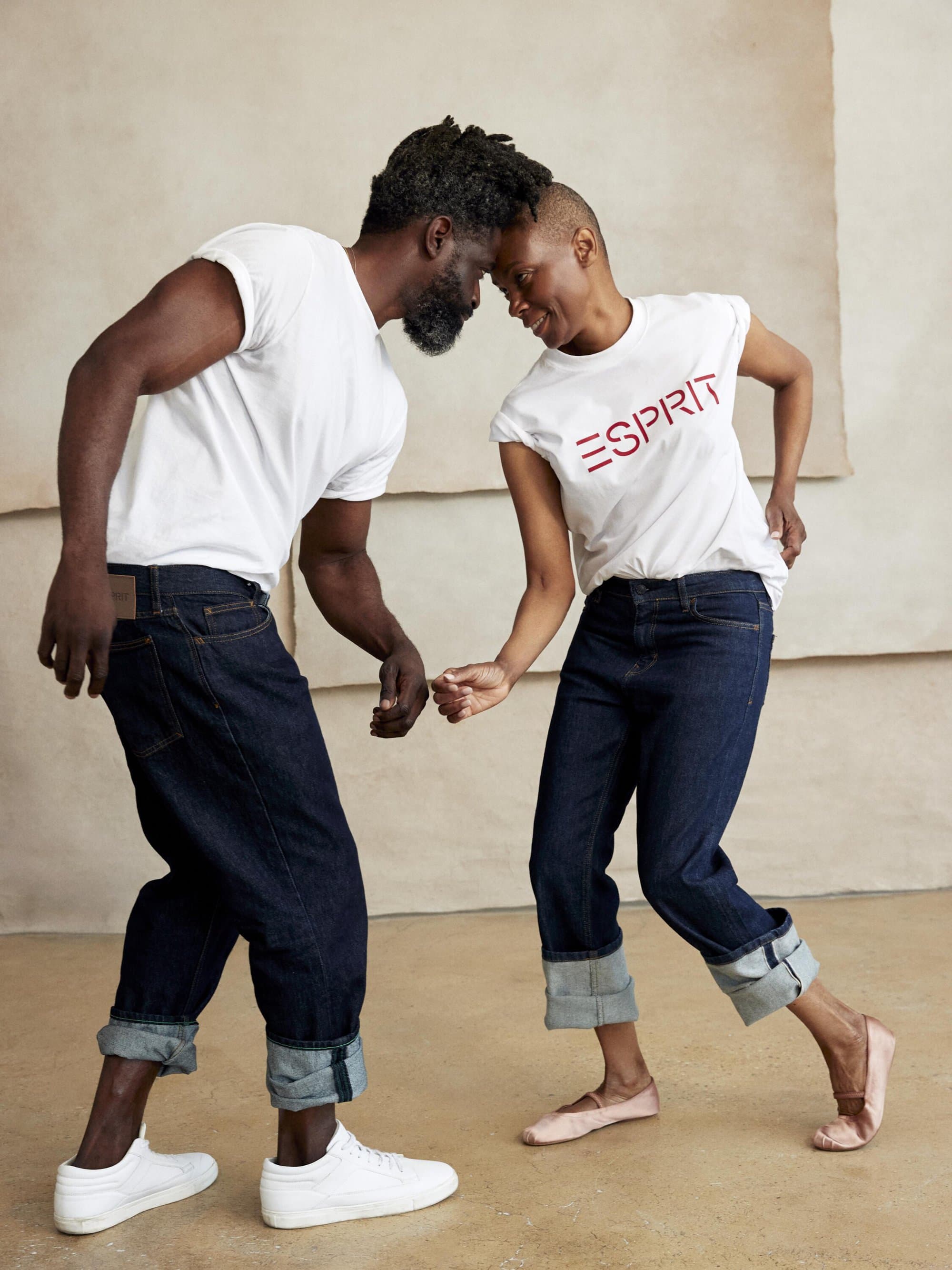 Two models in white t-shirts and cuffed dark denim jeans playfully touching foreheads in a studio campaign shoot.
