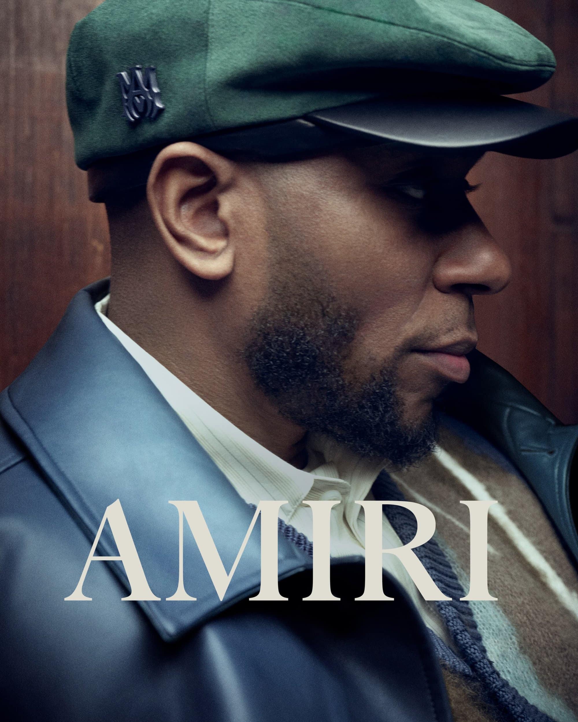 Close-up studio portrait of an adult male wearing a green cap and blue leather jacket, showcasing Amiri fashion brand clothing.