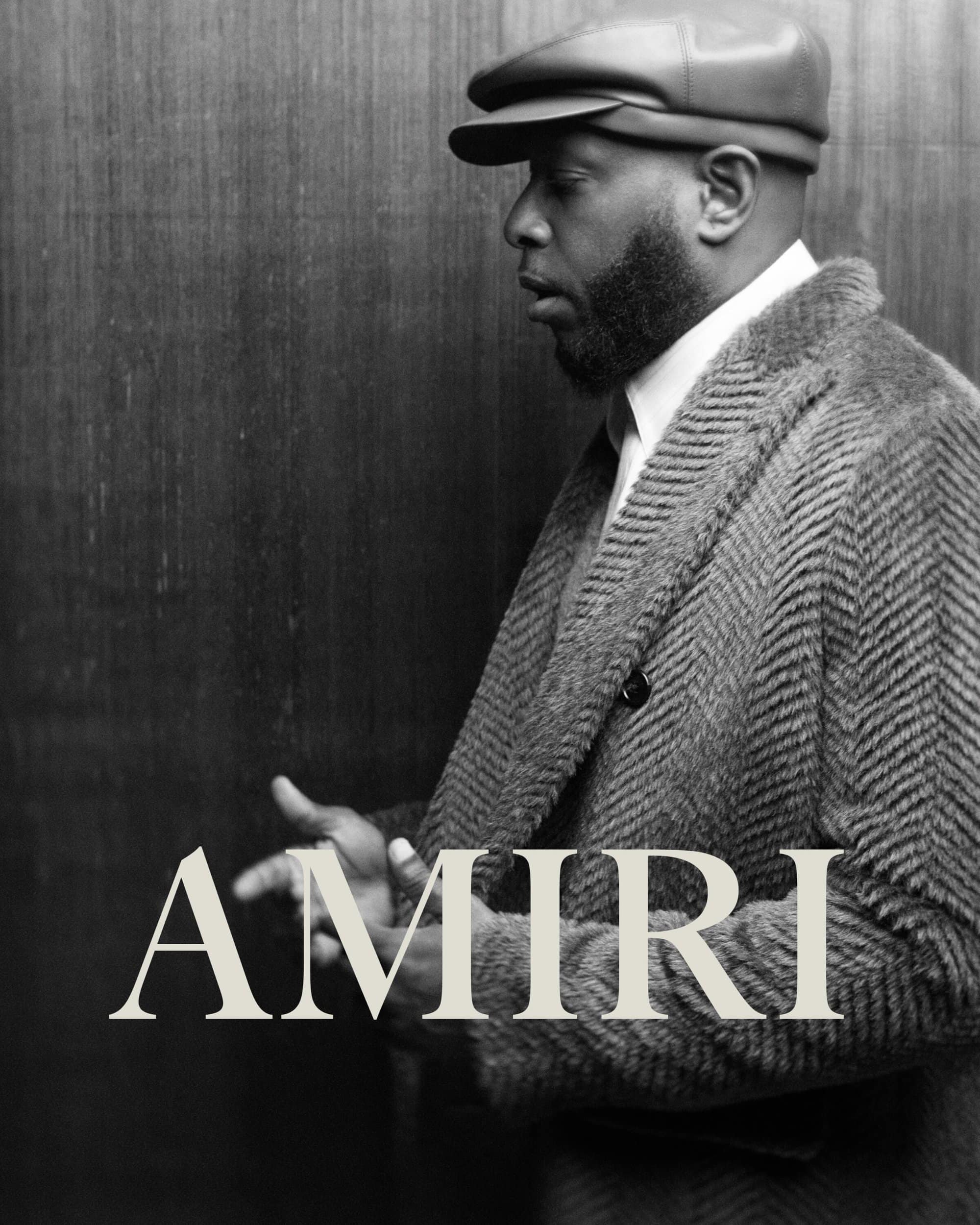 Black and white portrait of an African American man wearing a cap and herringbone coat, standing against a textured background.
