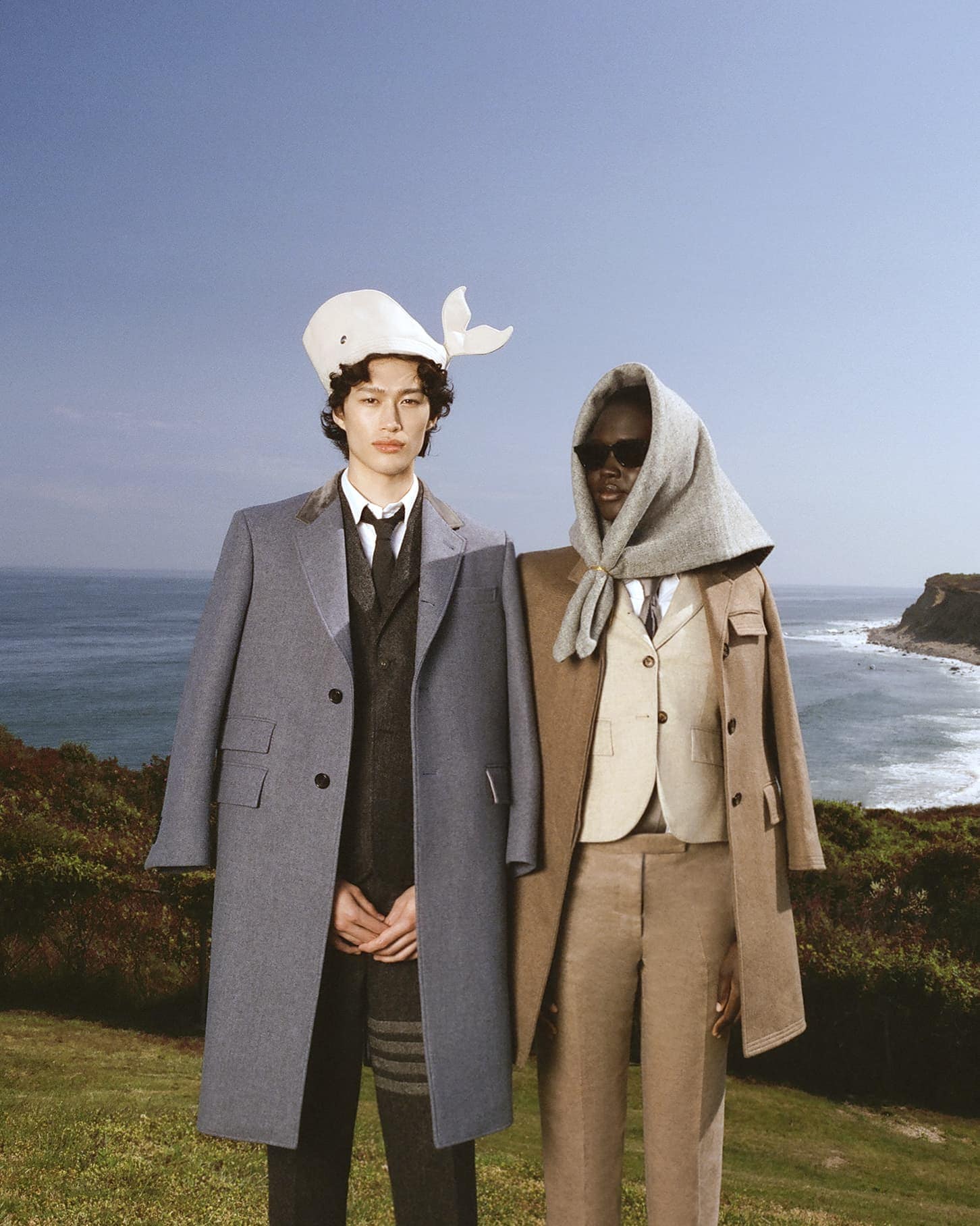 Two models wearing tailored Thom Browne winter coats outdoors against a coastal landscape background in Montauk.