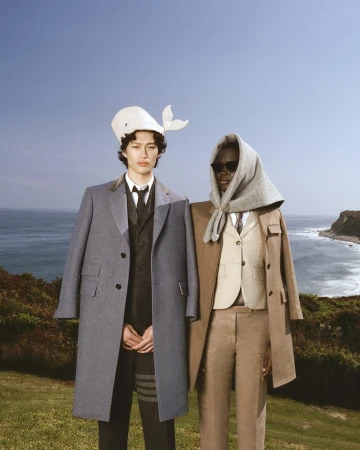 Two models wearing tailored Thom Browne winter coats outdoors against a coastal landscape background in Montauk.