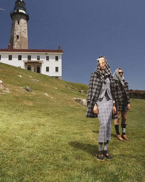 Two women in plaid outfits stand in a grassy field by a white lighthouse under a clear blue sky, fashion, style, and nature.