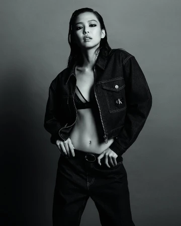 Jennie posing in an unbuttoned black denim jacket and bra for Calvin Klein against a studio backdrop.