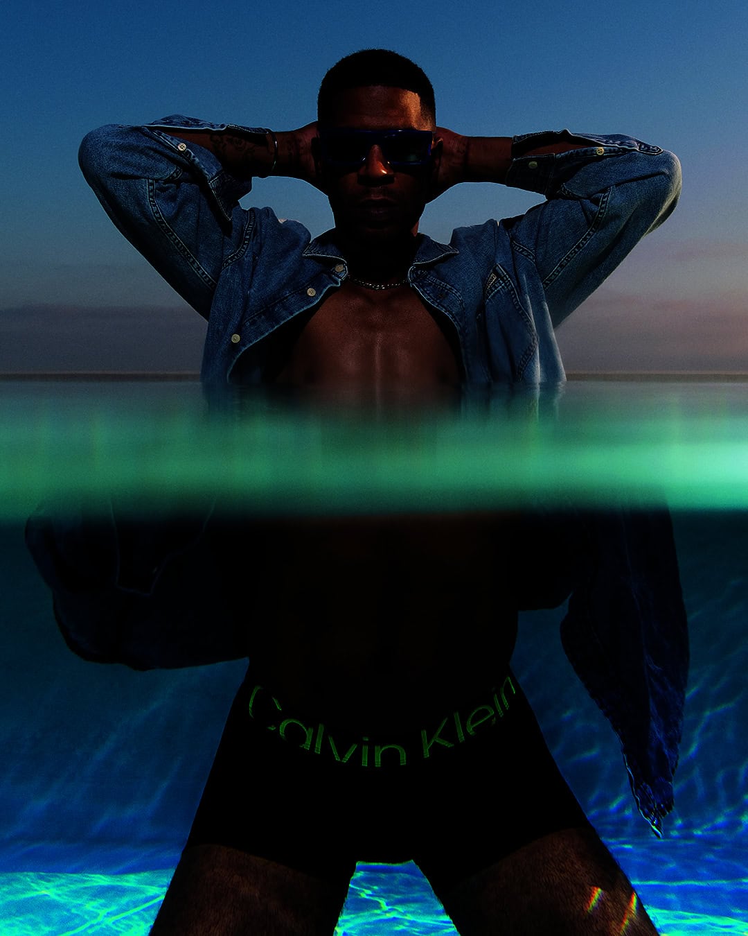 Kid Cudi wearing an unbuttoned denim shirt and Calvin Klein underwear, submerged waist-deep in water