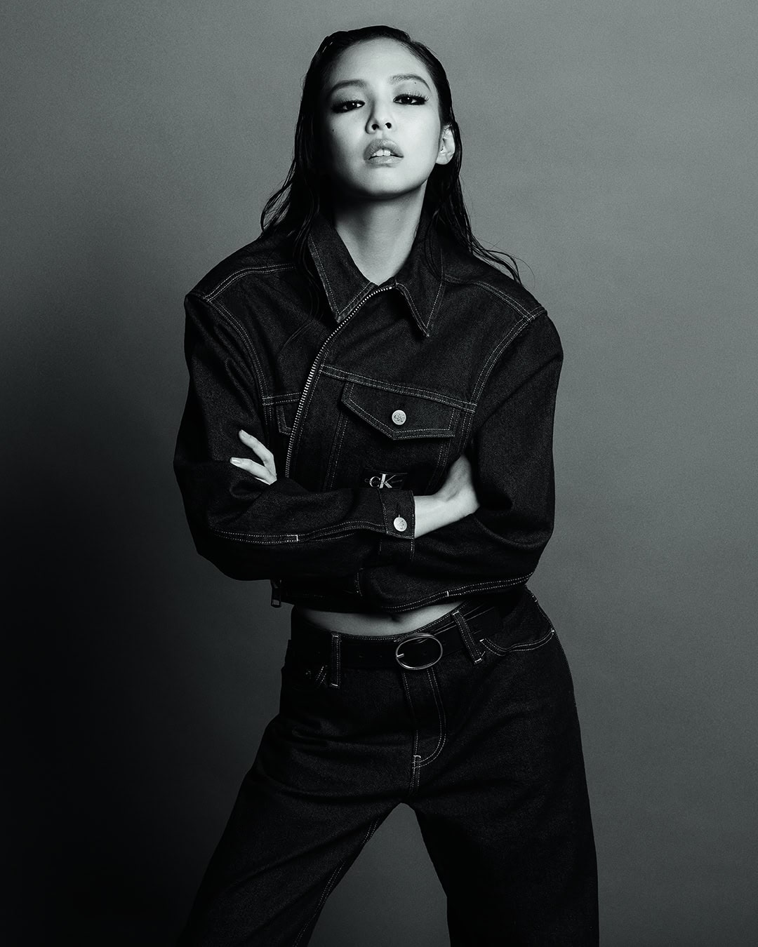 Jennie wearing a dark cropped denim jacket and matching jeans with arms crossed against a seamless studio backdrop.