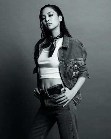 Jennie posing in a denim jacket and white tank top against a plain grey studio backdrop for Calvin Klein