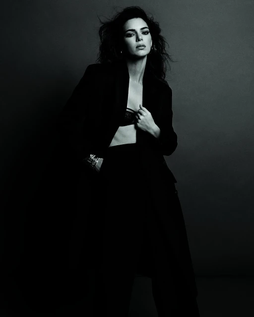 Elegant woman in black blazer and pants poses in a studio setting with dramatic lighting, showcasing a sophisticated fashion style.