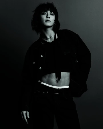 Jung Kook in dark jacket and jeans posing against dark background for Calvin Klein Fall 2023 campaign.