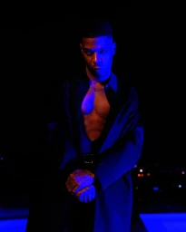 Kid Cudi in a dark open jacket illuminated by dramatic blue and red lighting for Calvin Klein Fall 2023 campaign.