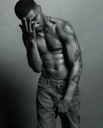 Black and white portrait of Kid Cudi wearing Calvin Klein underwear and jeans with tattooed arms.