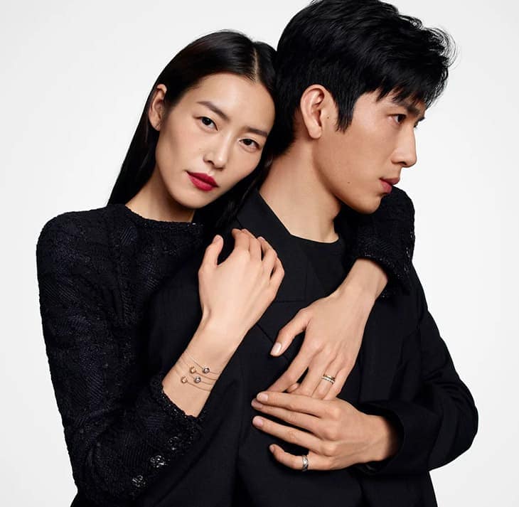 Elegant portrait of a stylish Asian couple embracing, woman with red lipstick and bracelet, man in a black suit against a bright backdrop.