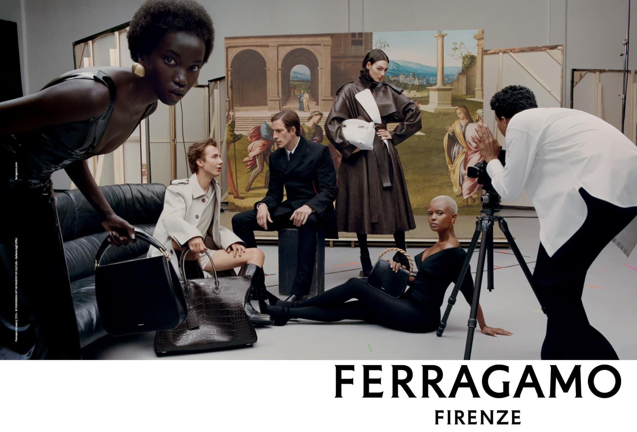 A diverse group of models pose in a photo studio showcasing Ferragamo handbags, with a photographer capturing the scene and a painted backdrop.