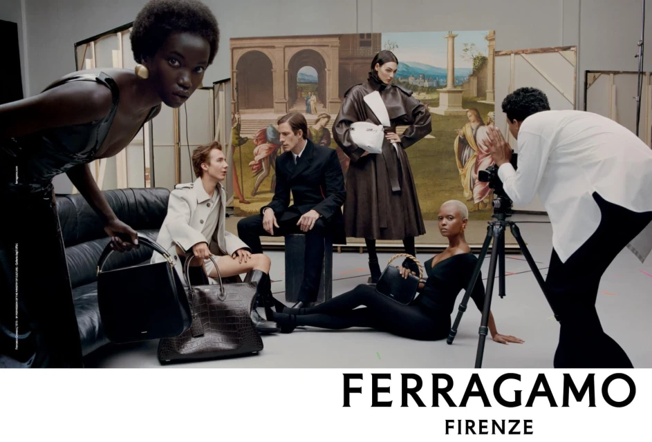 A diverse group of models pose in a photo studio showcasing Ferragamo handbags, with a photographer capturing the scene and a painted backdrop.