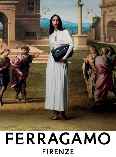 Elegant brunette woman in a white dress holds a black handbag in front of a Renaissance-style painting, fashion advertisement.