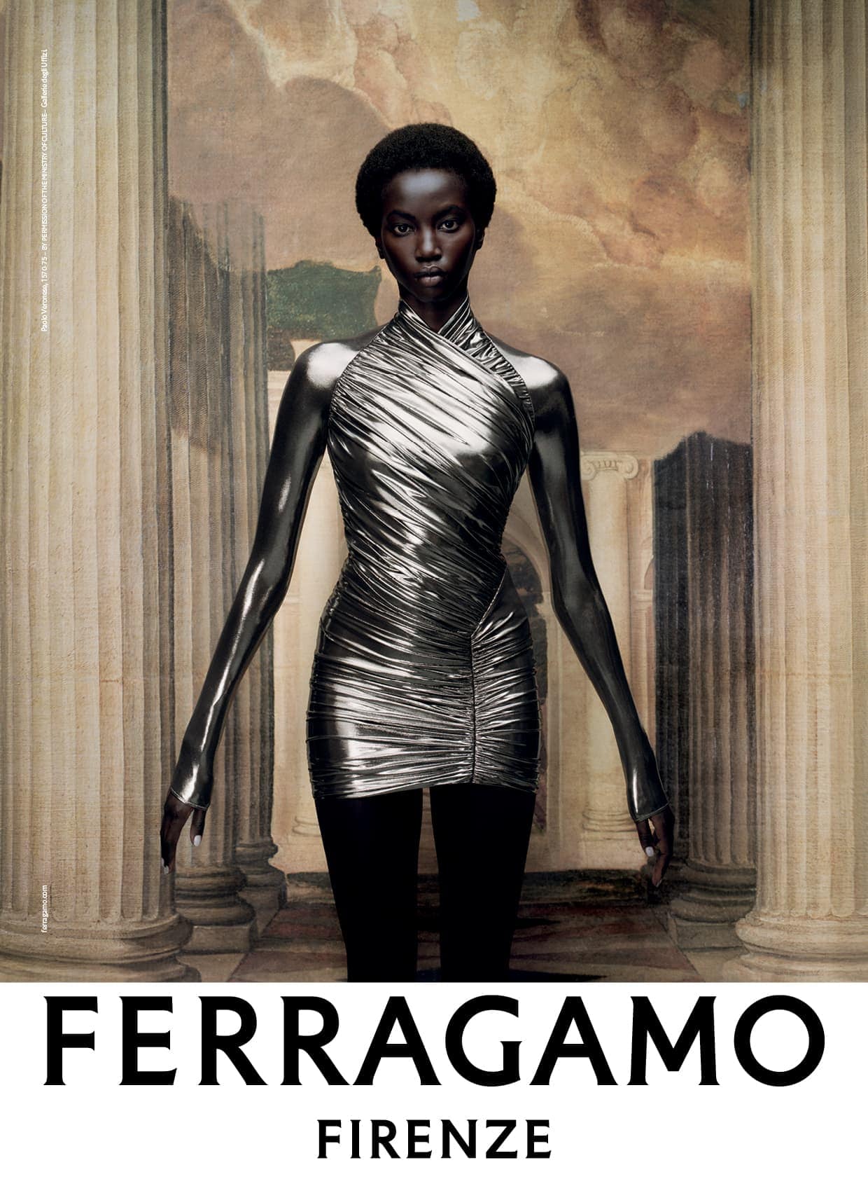 Fashion shot featuring a Black female model wearing a metallic dress in front of ancient columns and a painted sky backdrop.