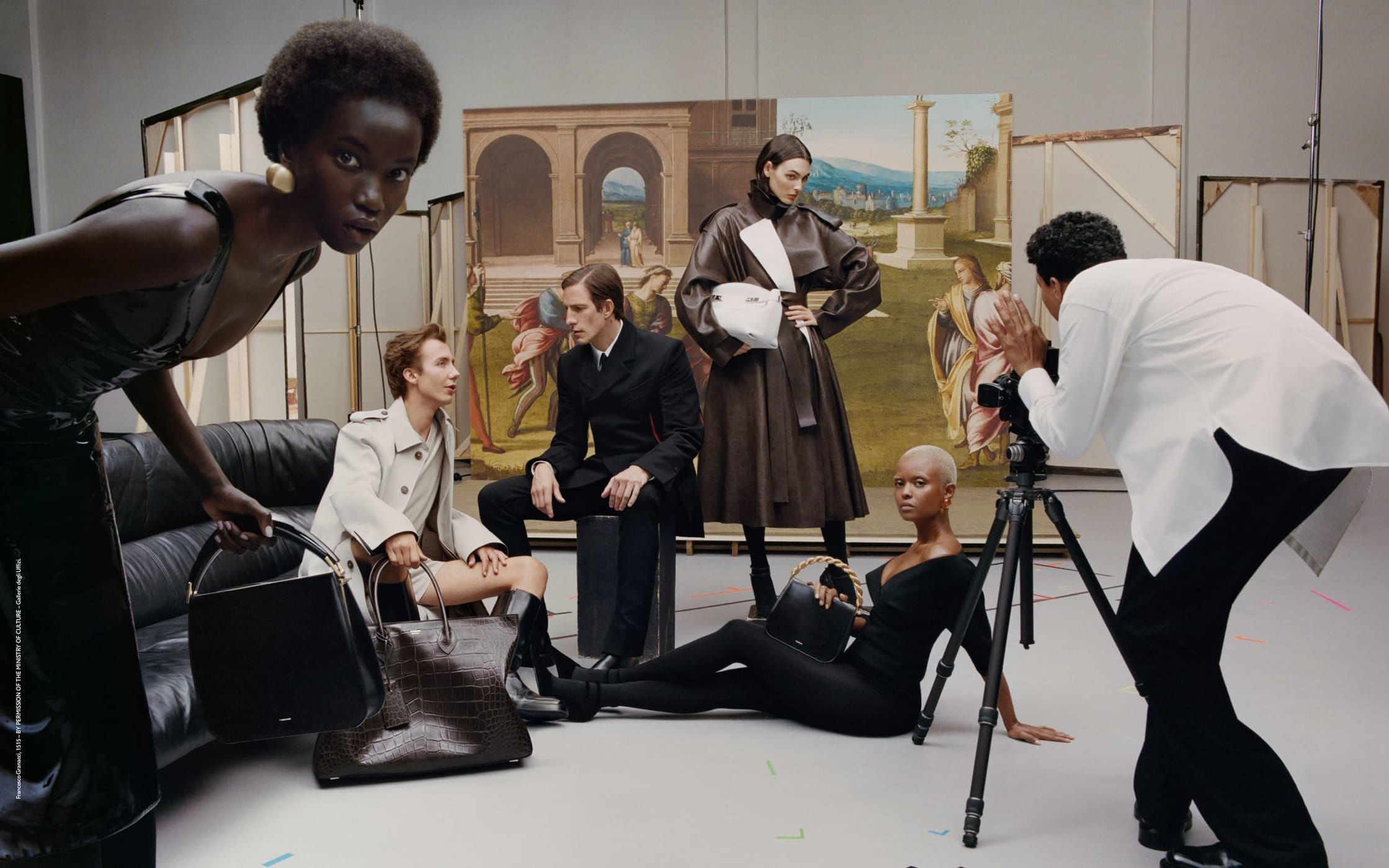 Fashion editorial featuring six diverse models in a studio setting with designer handbags and a photographer capturing the scene against a painted backdrop.