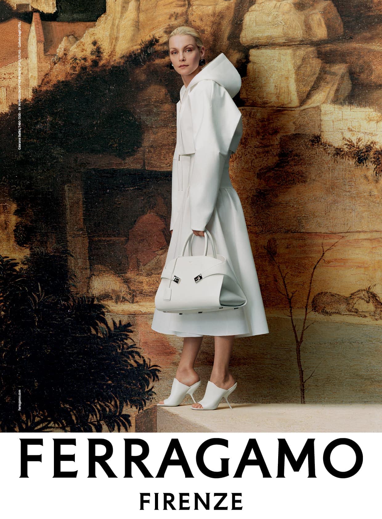 Elegant adult woman in a white hooded coat carrying a white purse and wearing white heels posing against a painted backdrop.