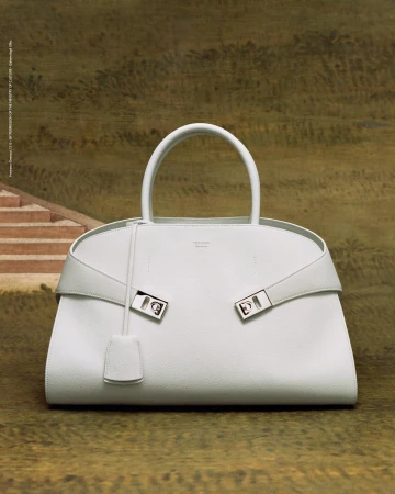 Elegant white leather handbag with silver hardware and top handle against a muted olive and beige scenic backdrop. Fashion accessory.