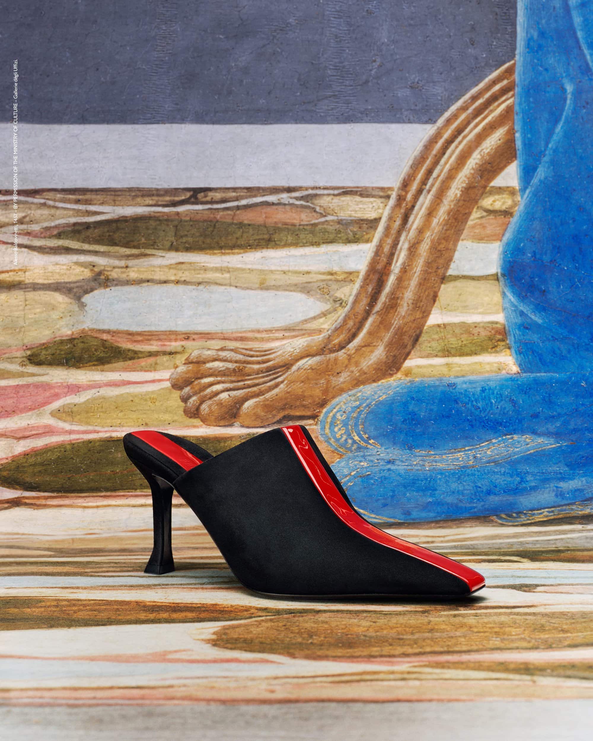 Black high-heeled mule with red trim on a painted surface featuring a seated figure, creating a visually striking fashion editorial.