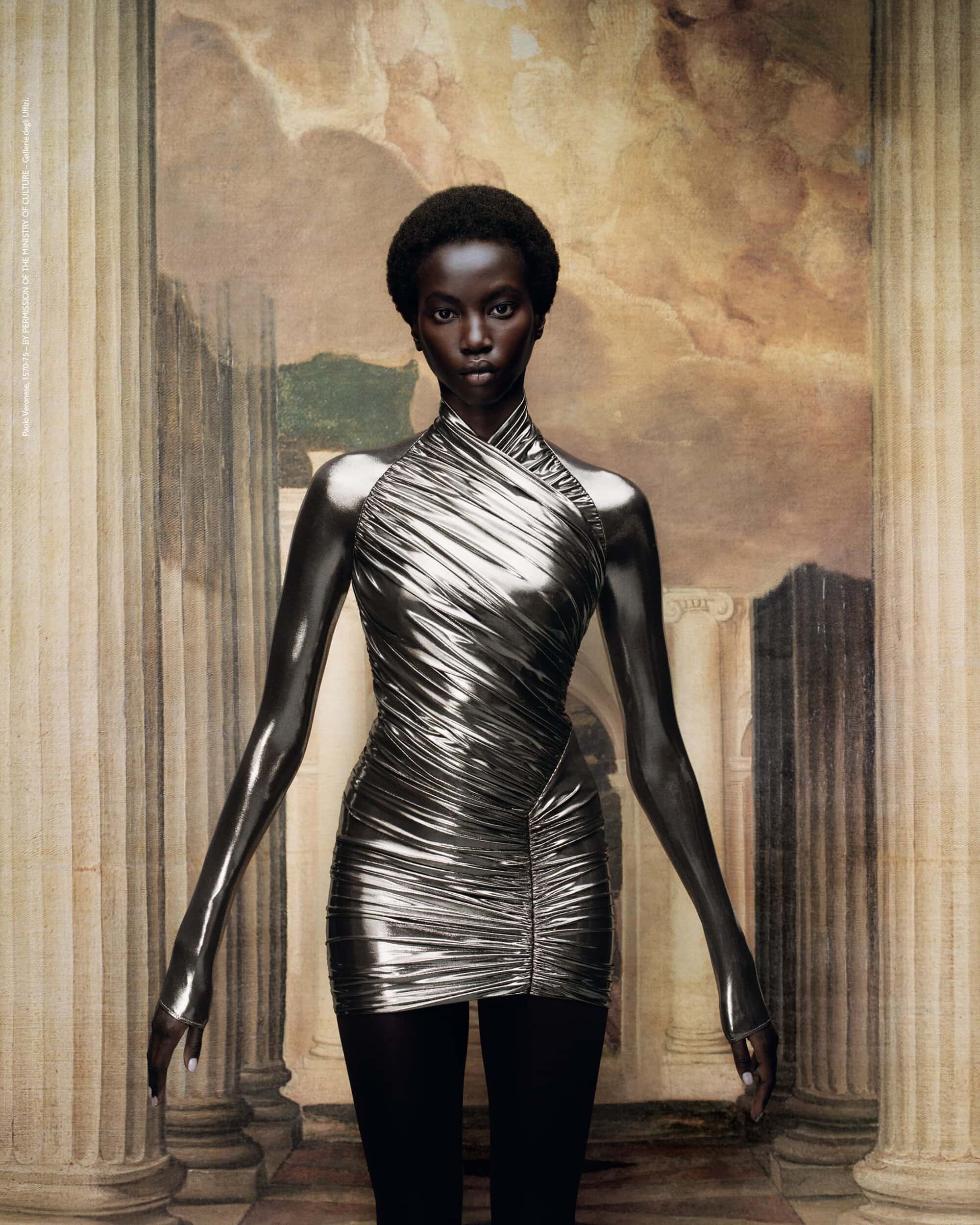 A fashion shot presents a poised African-descent woman in a metallic dress against a backdrop of ancient architectural elements and sky.