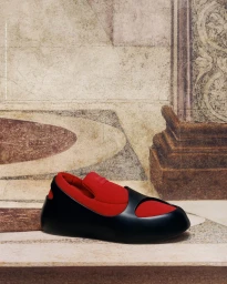 Ferragamo red and black sculptural slip-on shoe resting against an Italian Renaissance painting backdrop.