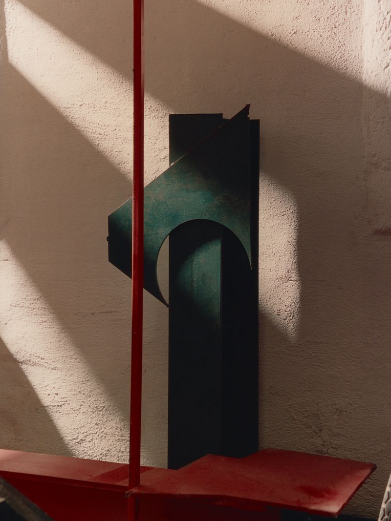Abstract sculpture featuring geometric shapes and a primary red color scheme against a textured beige background with soft shadow patterns.