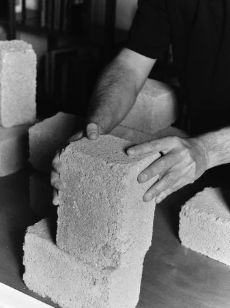 Hands arranging cinder blocks on a table, black and white photo. Construction or artistic expression. Indoor setting, books in background.