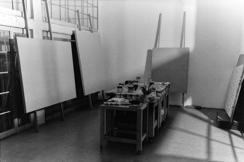 Bright photo studio with blank canvases on easels, a table with paint supplies, and natural light streaming through the windows.