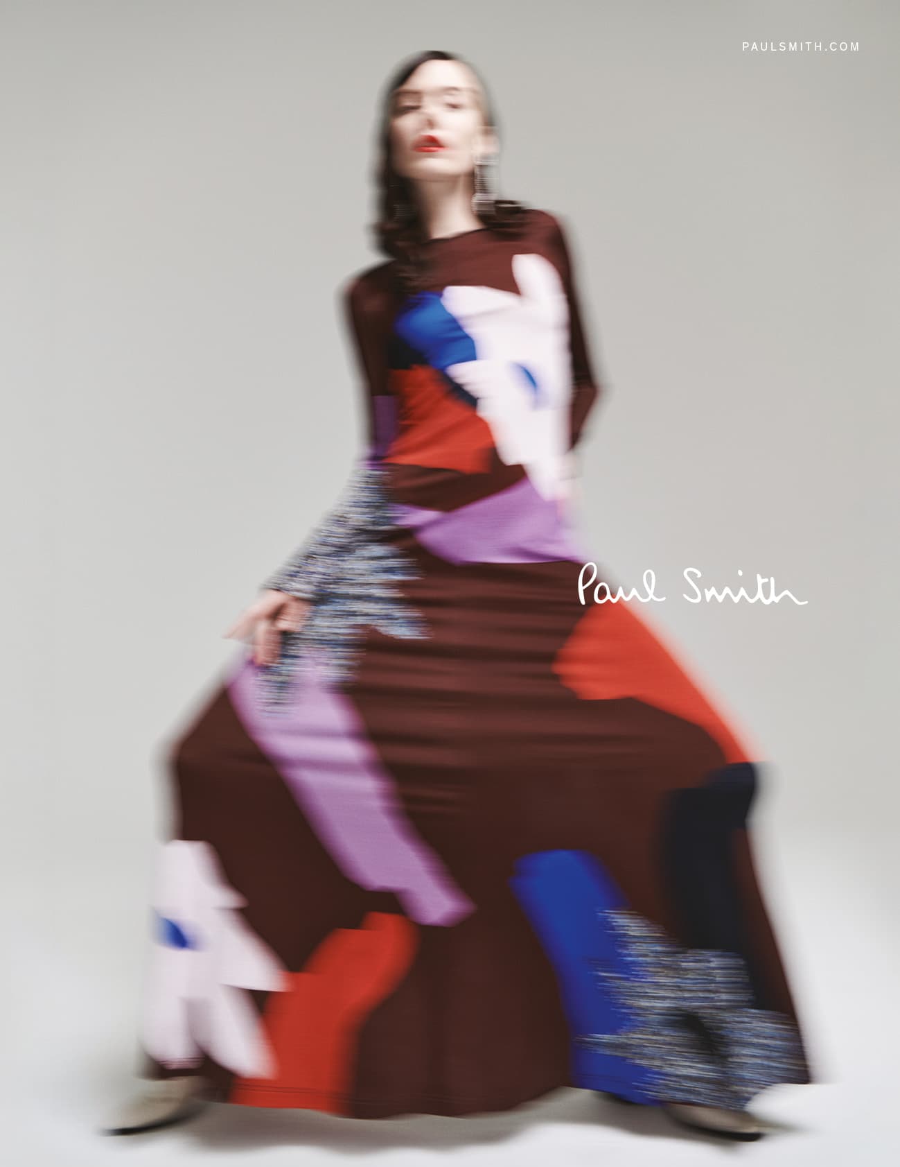 Fashion shot of a model in a Paul Smith long-sleeved gown, with a brown bodice and a multicoloured skirt, against a neutral studio background.