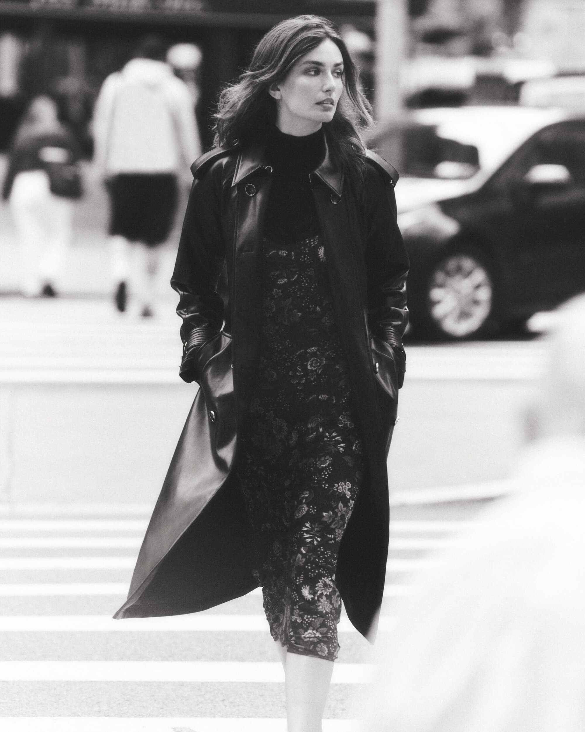 Fashionable adult female walking across a crosswalk in a city street, wearing a stylish black coat and dress.